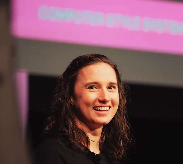 A smiling conference attendee in front of a pink presentation screen.
